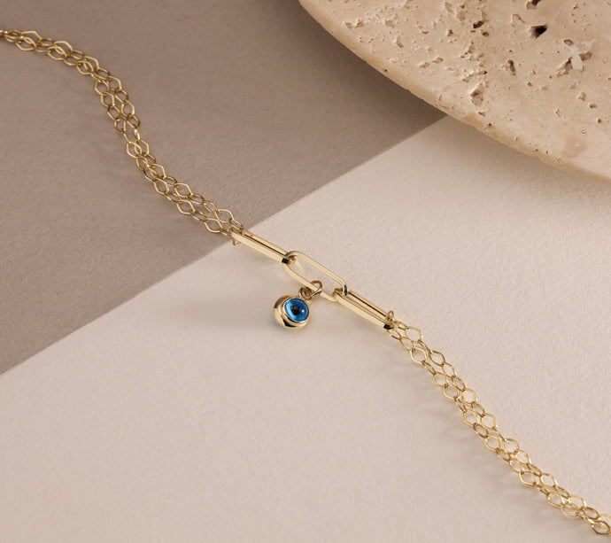 Gold bracelet with a blue evil eye charm on a beige background
